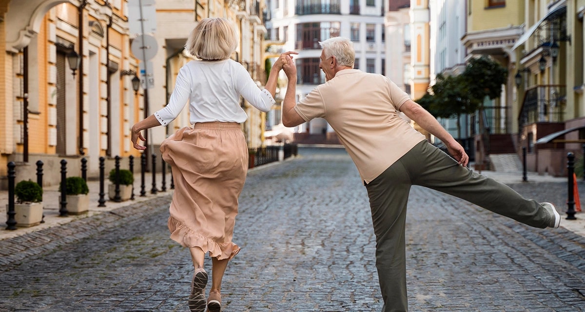 An old couple walks along a street while dancing
